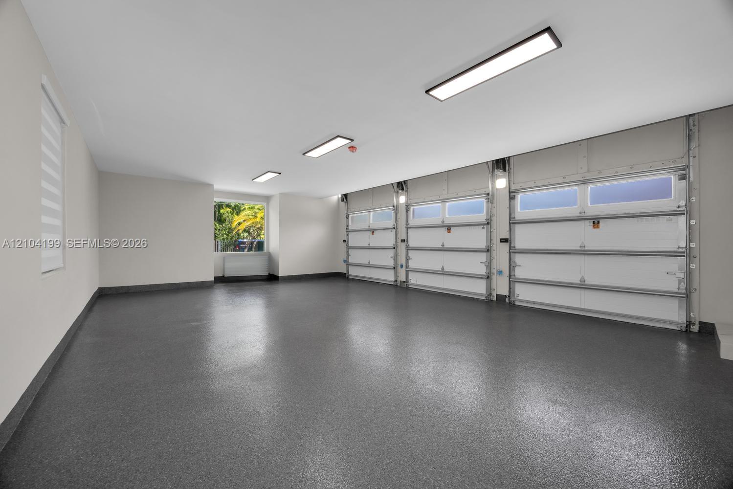 Three-car garage featuring a speckled epoxy-coated floor, bright LED panel lighting, and three sectional garage doors with frosted windows