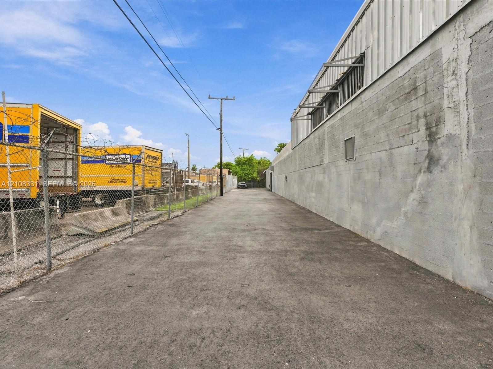 Paved exterior access drive featuring concrete block wall construction and chain-link perimeter fencing