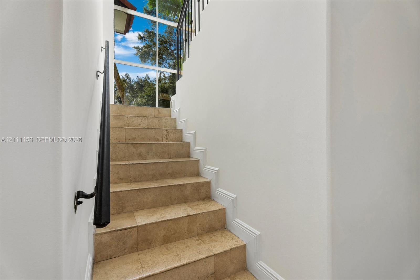 Staircase featuring natural stone treads, wrought iron railing, and floor-to-ceiling windows