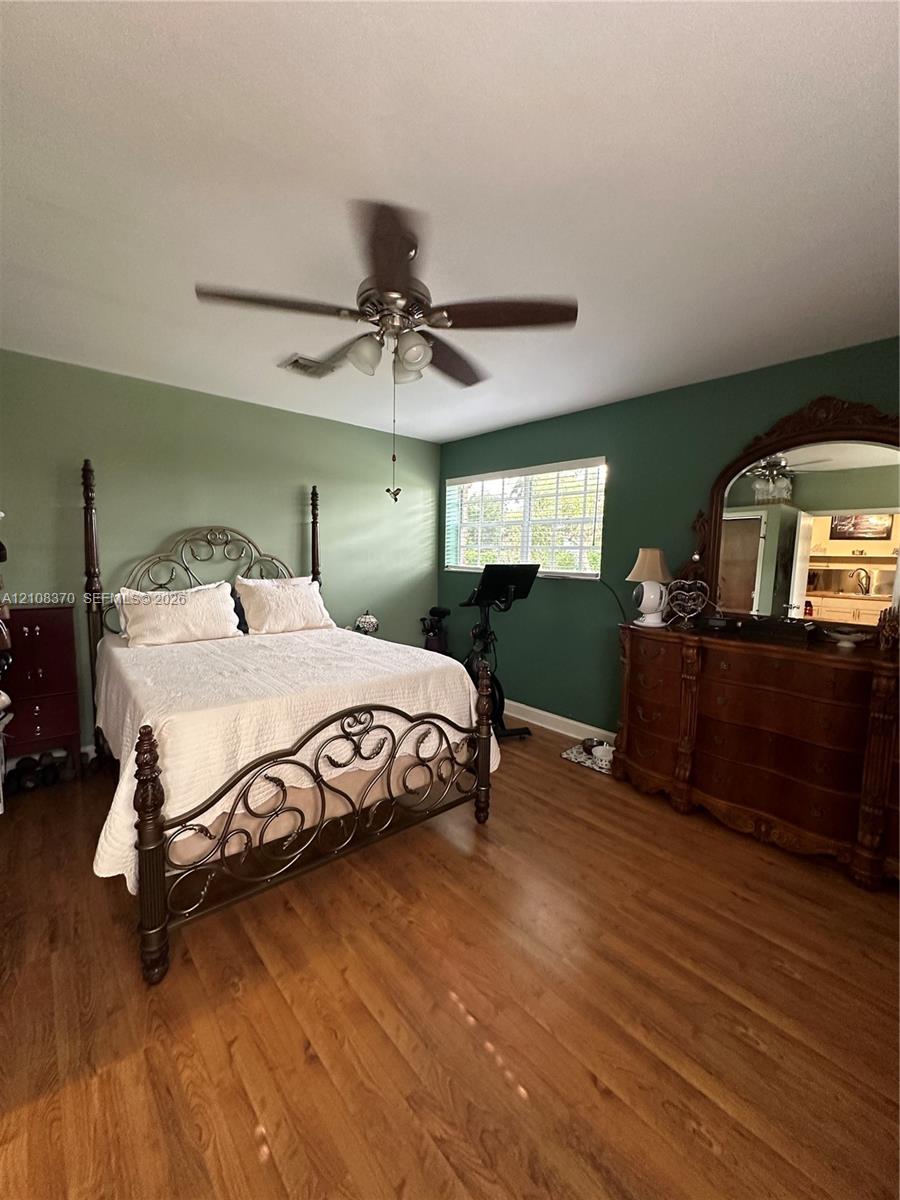 Room featuring wood-finish flooring, a multi-blade ceiling fan with integrated light fixture, and a single-pane window with a grid pattern