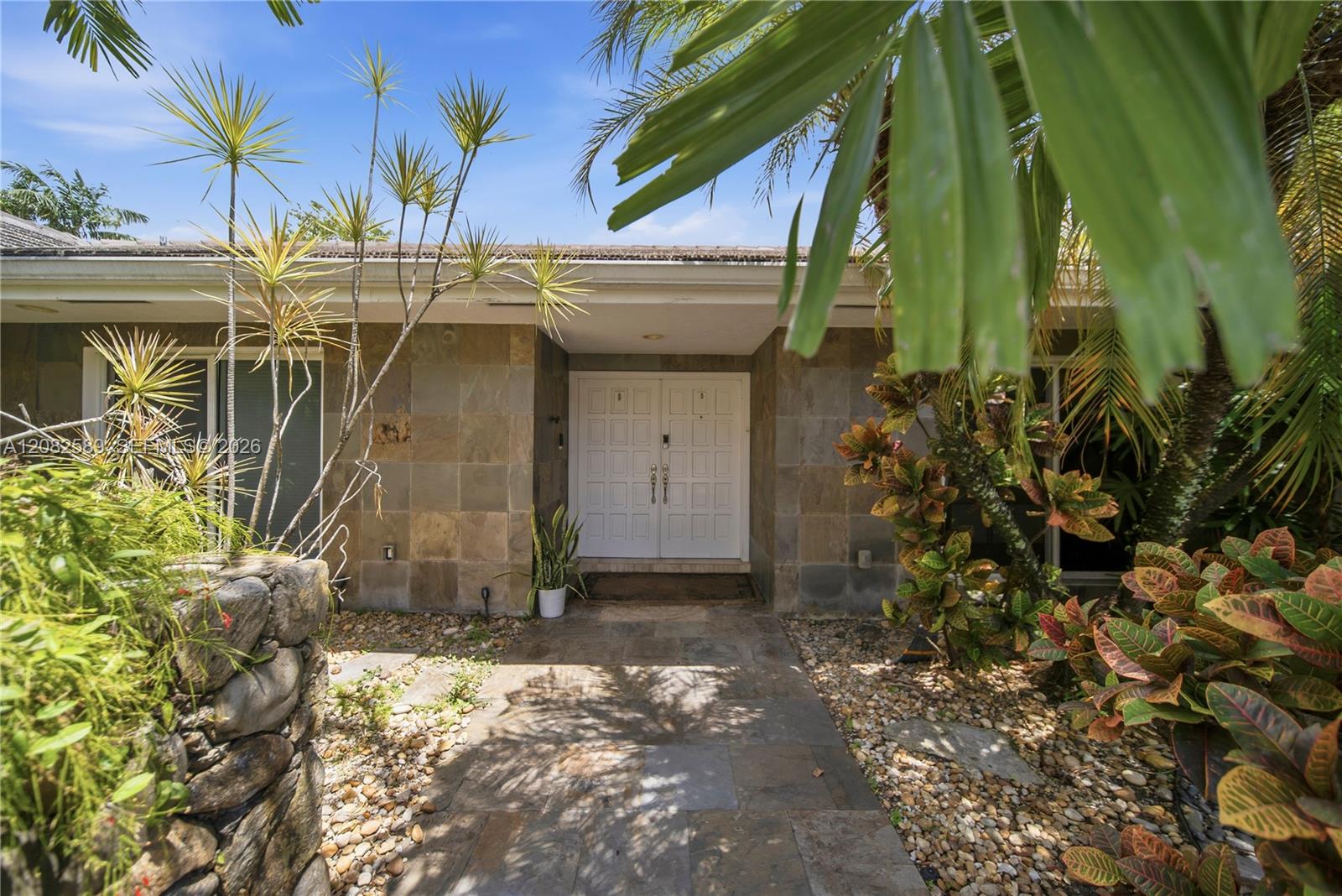 Elegant covered entrance surrounded by lush tropical landscaping, creating a warm and private welcome.