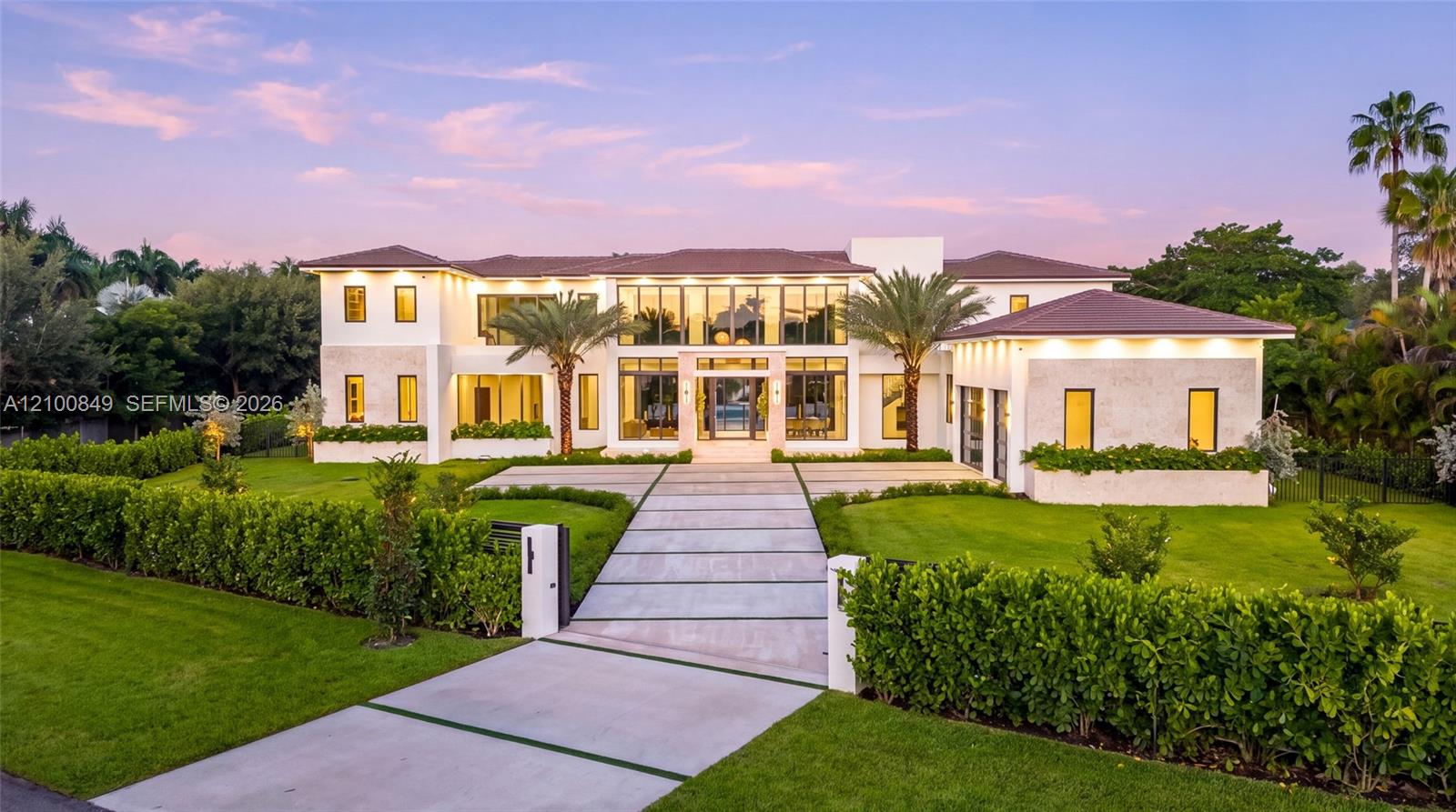 Contemporary two-story estate featuring a smooth stucco exterior, floor-to-ceiling glass windows, wide paver driveway, and manicured landscaping
