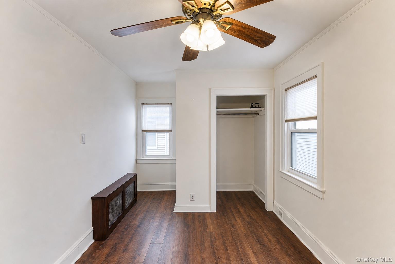 Recessed closet opening, wood-finish flooring, two windows with blinds, and ceiling fan with integrated lighting