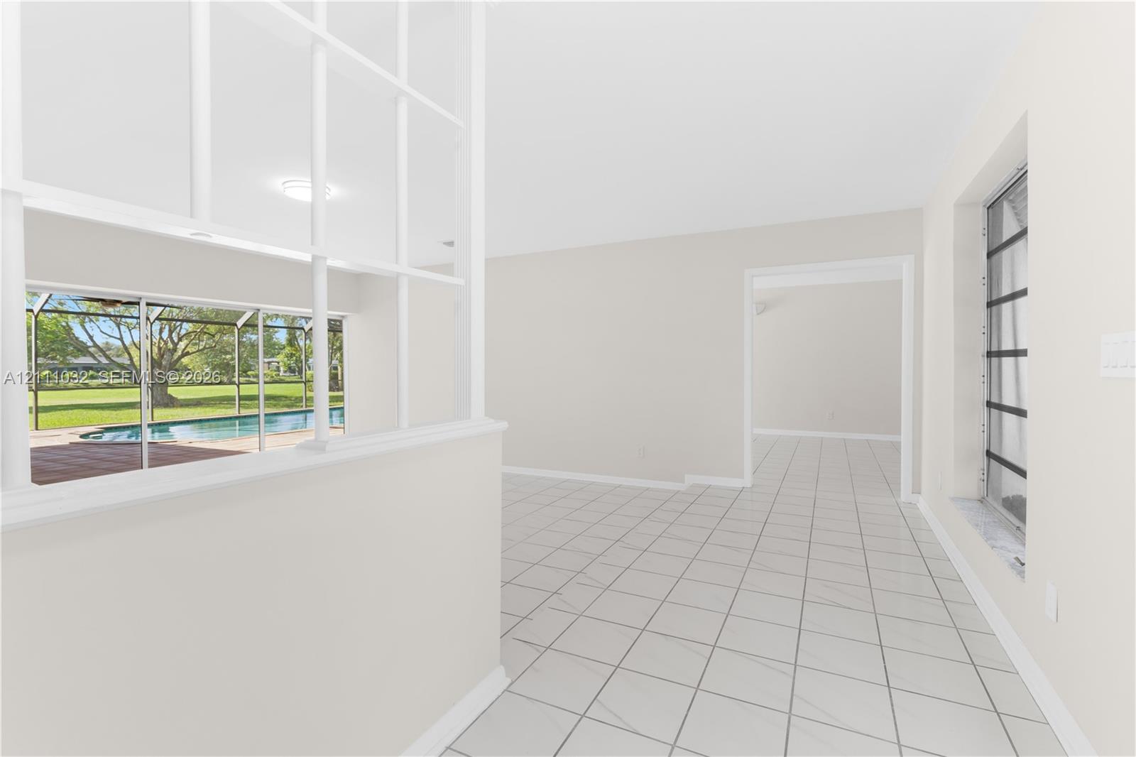 Interior space featuring white ceramic tile flooring, a half-wall with a white-frame glass partition, and large windows with horizontal mullions