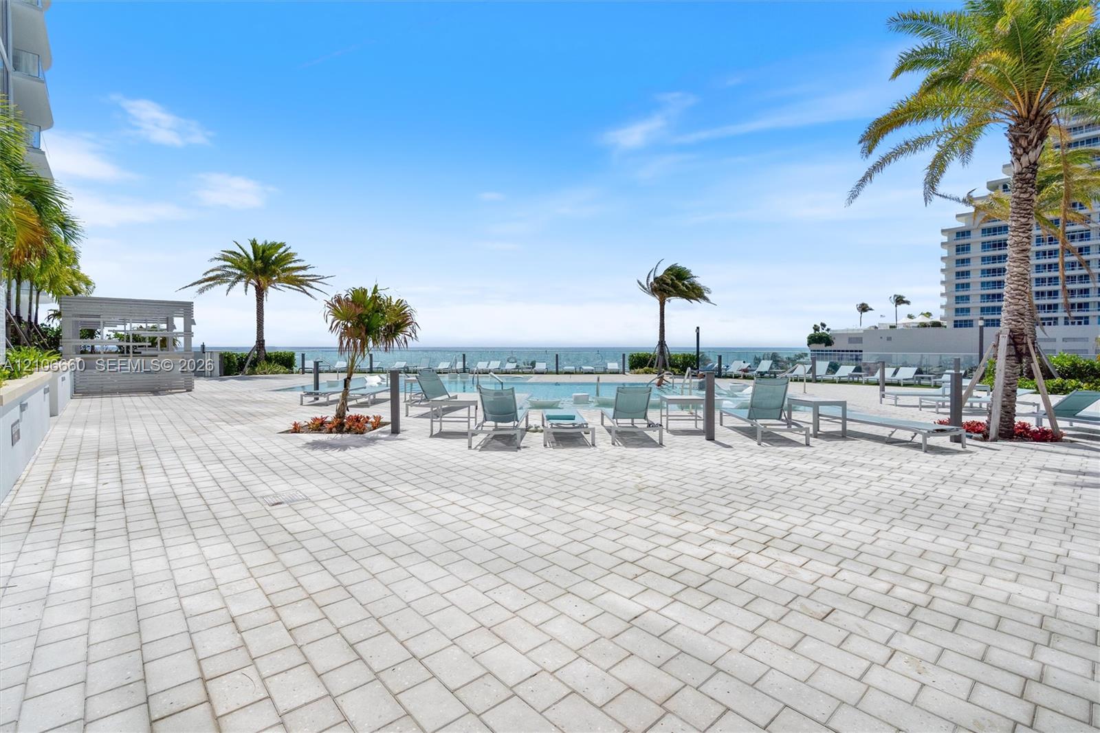 Outdoor swimming pool featuring stone-paver decking, mature palm trees, and a glass-paneled perimeter railing overlooking the ocean