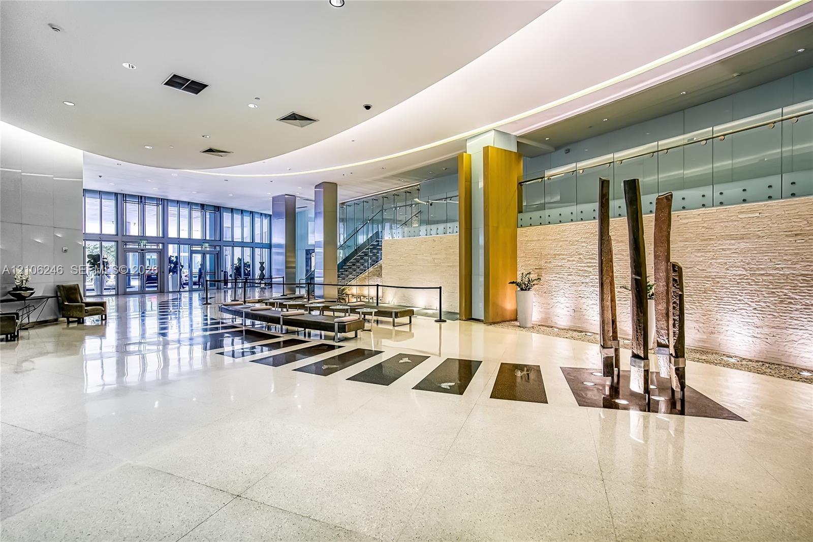 Grand lobby featuring polished stone flooring, curved recessed ceiling lighting, full-height floor-to-ceiling windows, stacked-stone accent wall, and 