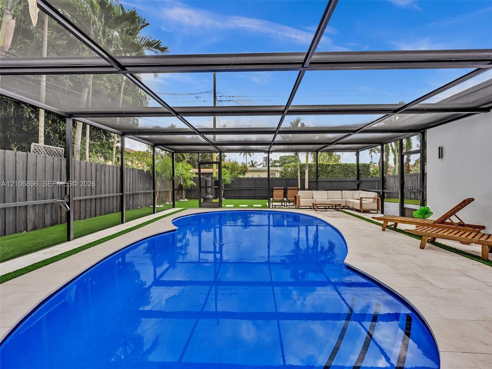 Screened-in outdoor living area featuring a custom-shaped swimming pool, paved pool deck, and synthetic turf lawn bordered by perimeter fencing