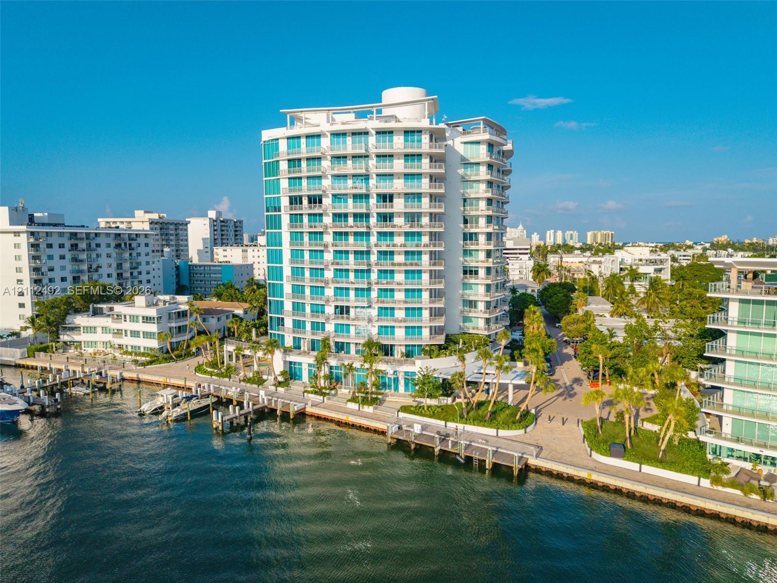 High-rise waterfront building featuring floor-to-ceiling glass paneling, tiered private balconies, an integrated deep-water dock, and paved perimeter 
