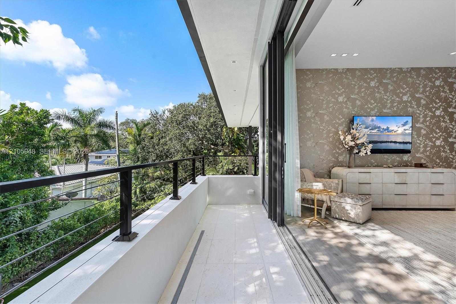 Covered balcony with stone-tile flooring and black metal railing featuring horizontal cable infill, highlighted by large-format retractable glass door