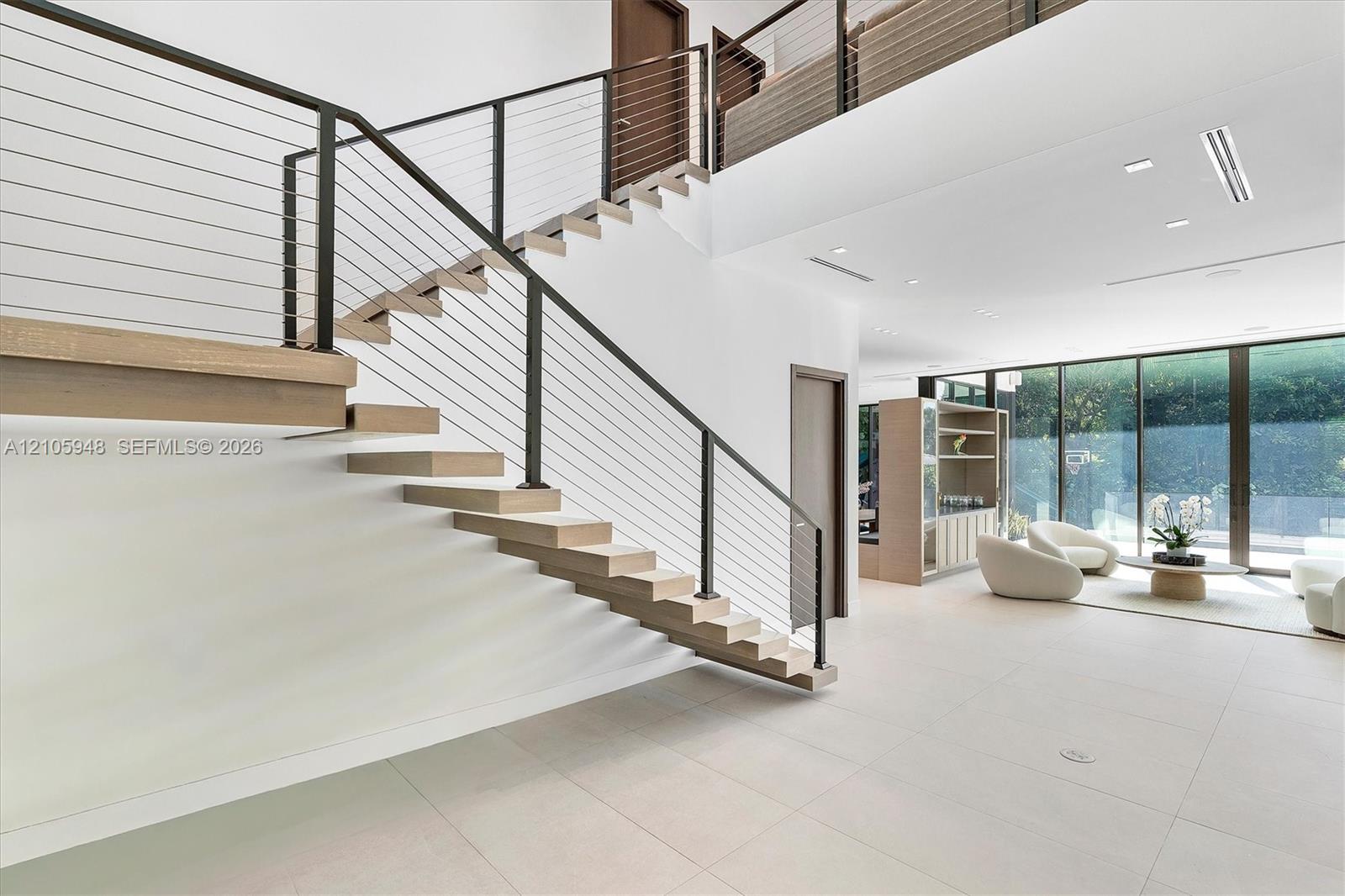 Floating staircase with wood-finish treads and horizontal cable railing, large-format tile flooring, and expansive floor-to-ceiling glass wall panels