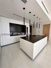 Modern kitchen featuring white flat-panel cabinetry, a central island with a dark countertop, recessed lighting, and a series of minimalist pendant li