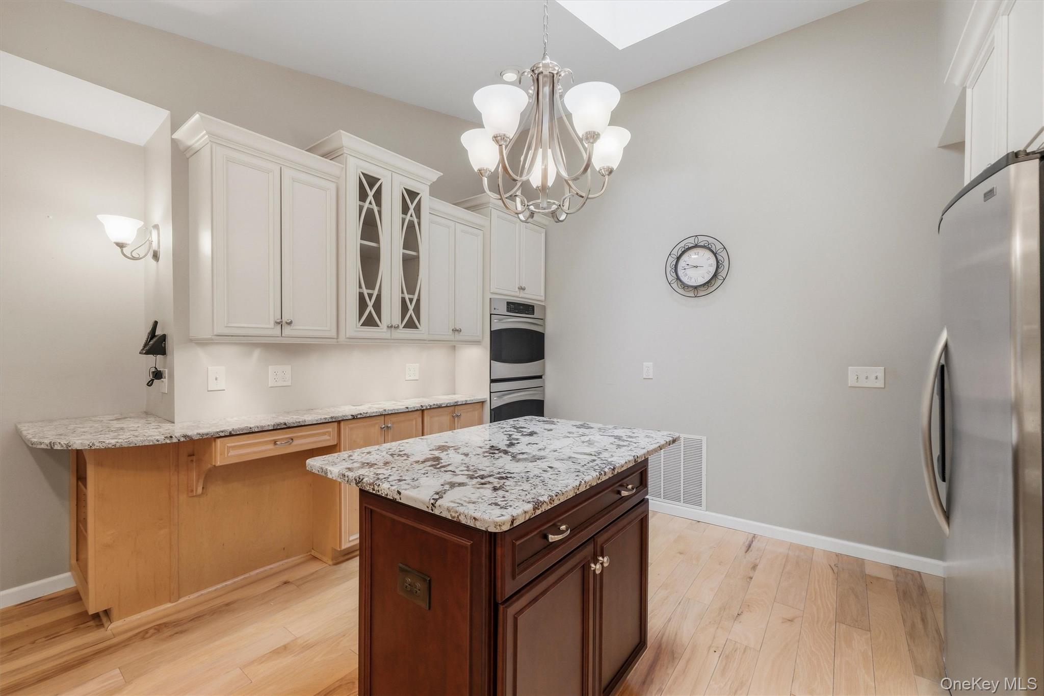 Custom kitchen with center island and snack bar, stainless appliances including double ovens, granite counters and wood floors