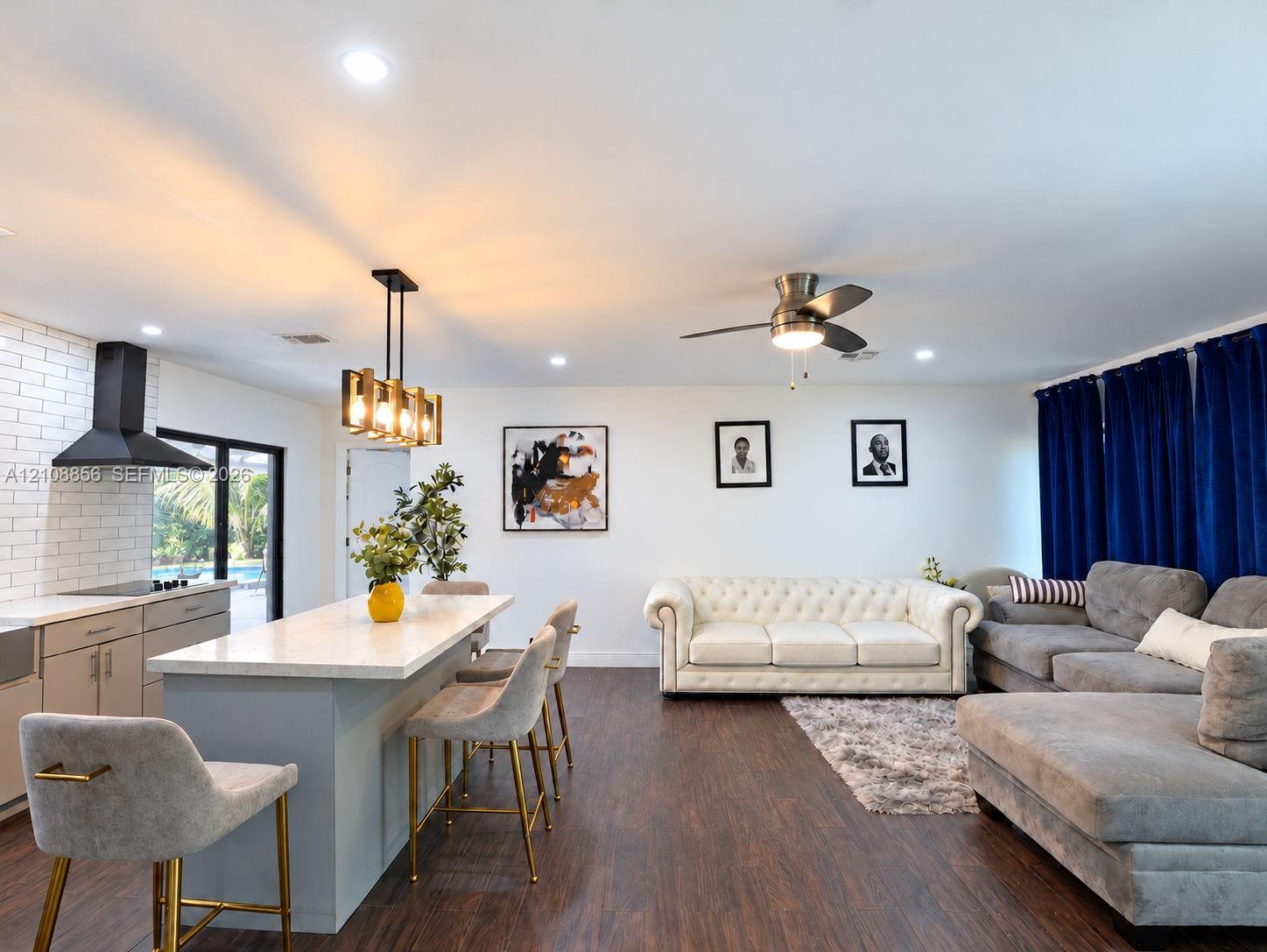 Open-concept kitchen and living area featuring a center island with light-toned solid surface countertop, white brick backsplash, matte black range ho