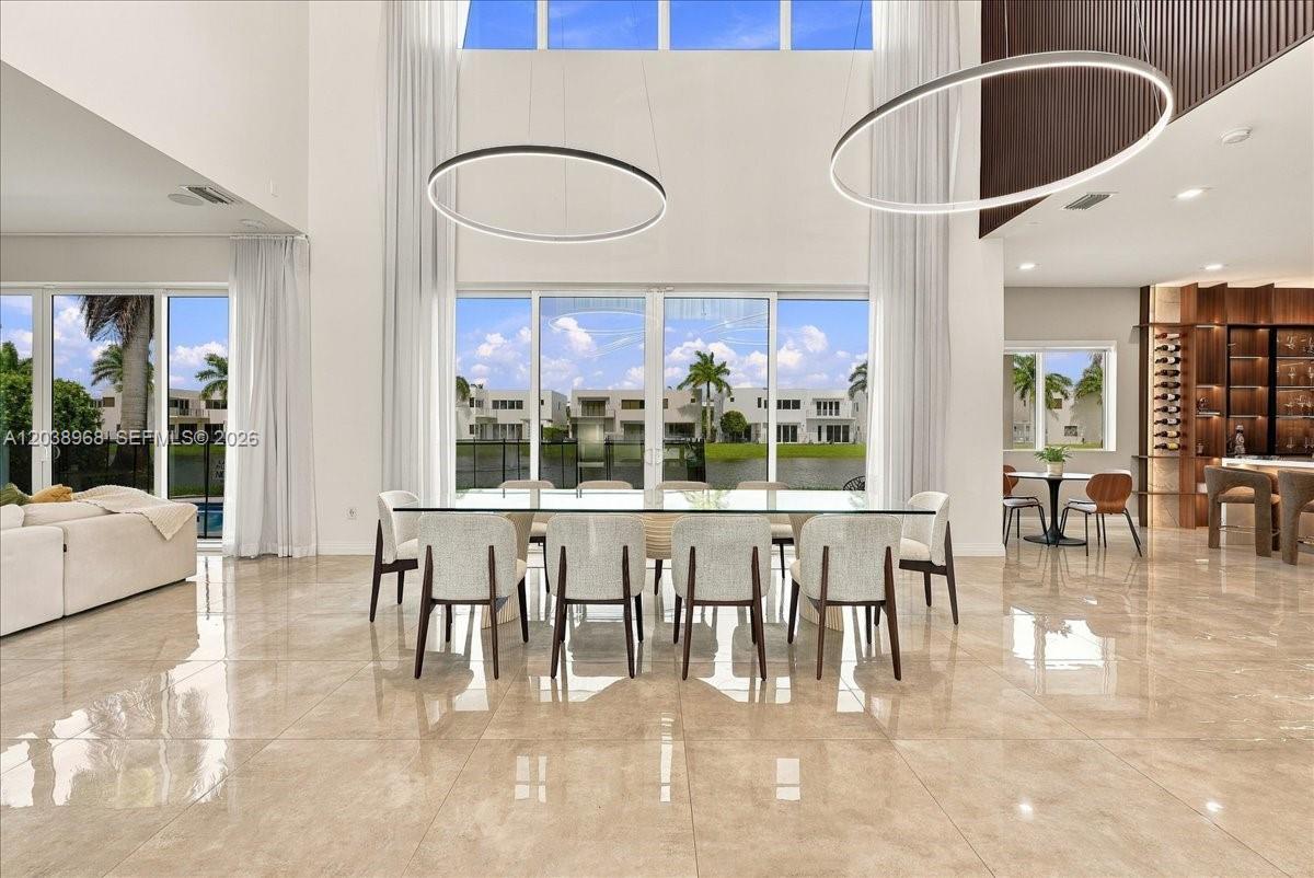 Double-height ceilings with expansive floor-to-ceiling glass, polished stone tile flooring, large-scale circular pendant lighting, and a custom built-