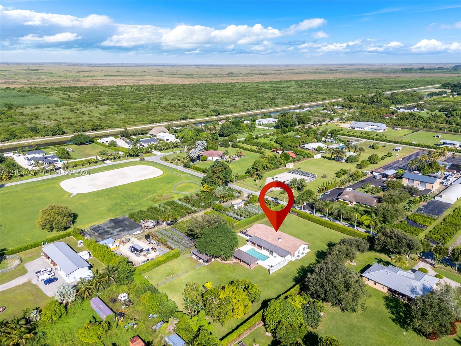 Aerial perspective featuring a sprawling parcel with expansive green space, a paved driveway, and an in-ground swimming pool