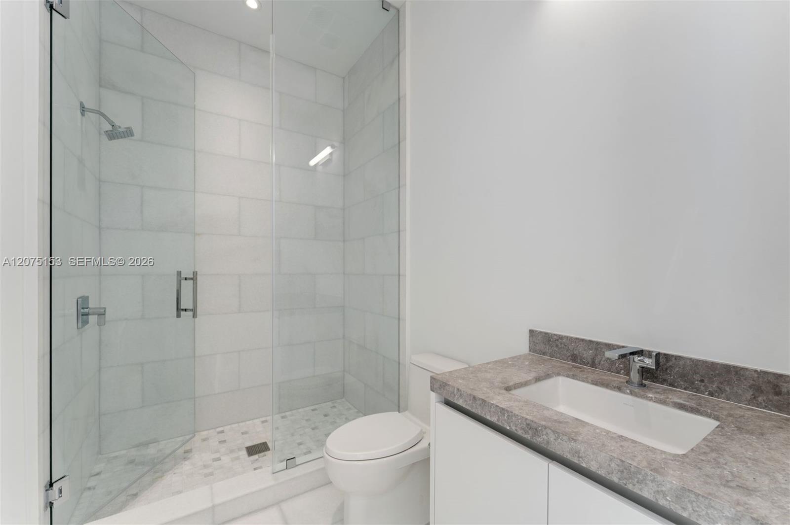 Walk-in shower with floor-to-ceiling tile, frameless glass enclosure, and stone-finish vanity countertop with integrated rectangular basin