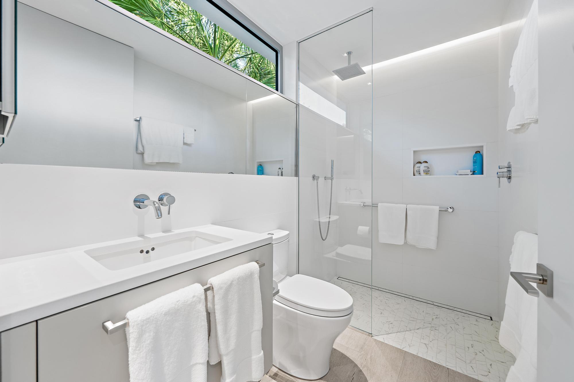 Modern bathroom featuring a vanity with an integrated sink, polished chrome wall-mounted faucet, a flush-mounted toilet, and a glass-enclosed shower w