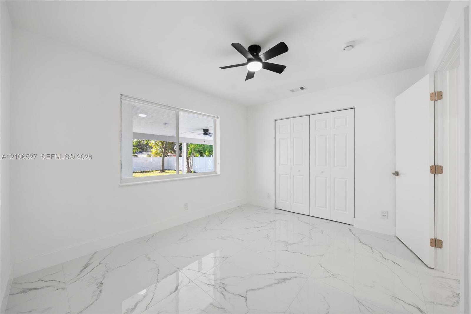 Interior space featuring large-format tile flooring with a neutral veined pattern, dual-panel closet doors, and a matte black ceiling fan with an inte
