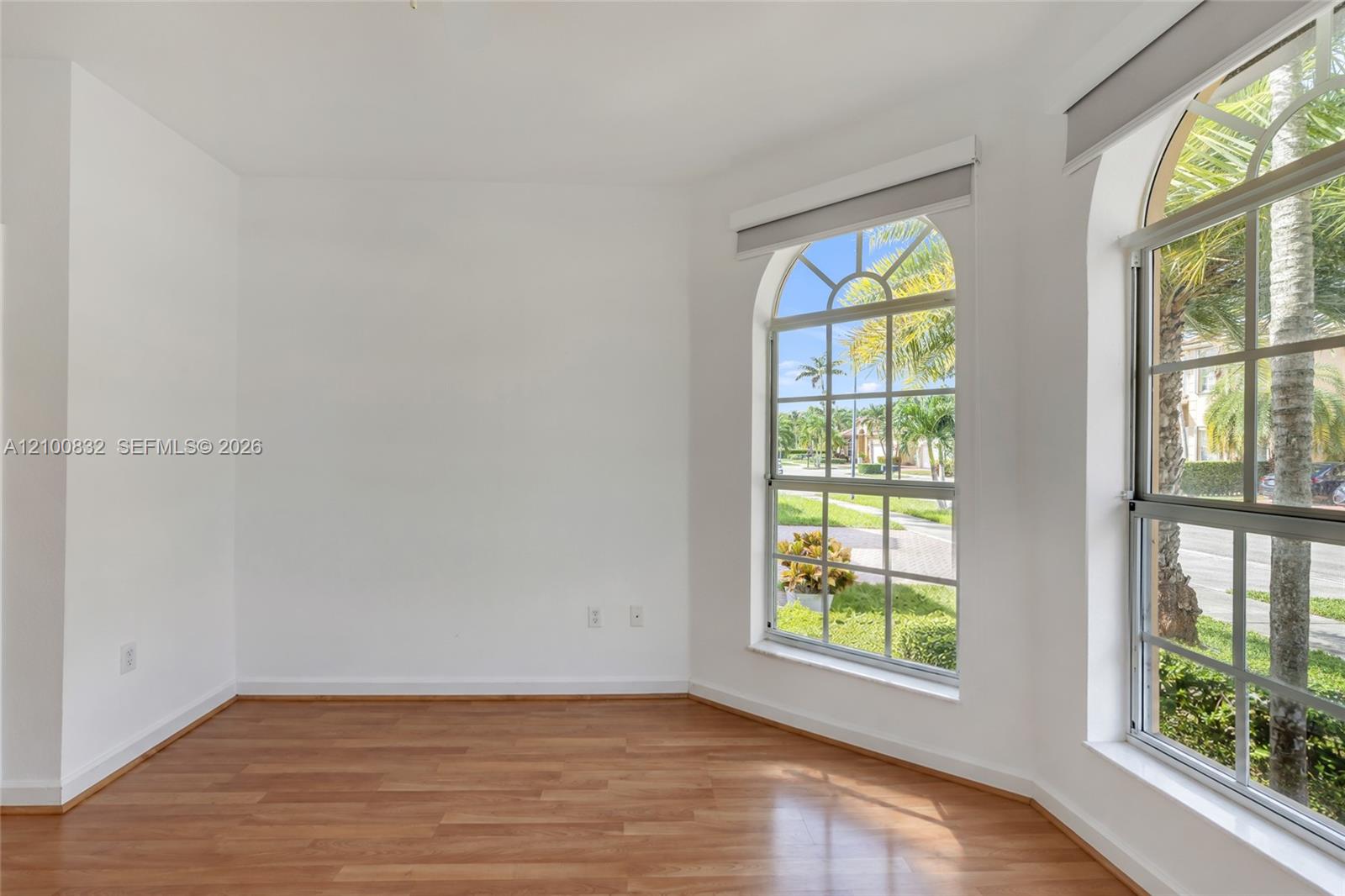 Room featuring wood-finish flooring, two large arched windows, and crisp white wall finishes