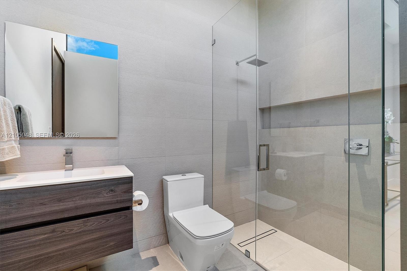 Floating vanity with wood-finish cabinetry, rectangular vessel sink, wall-to-wall mirror, glass-enclosed shower with rainfall showerhead, and wall-mou
