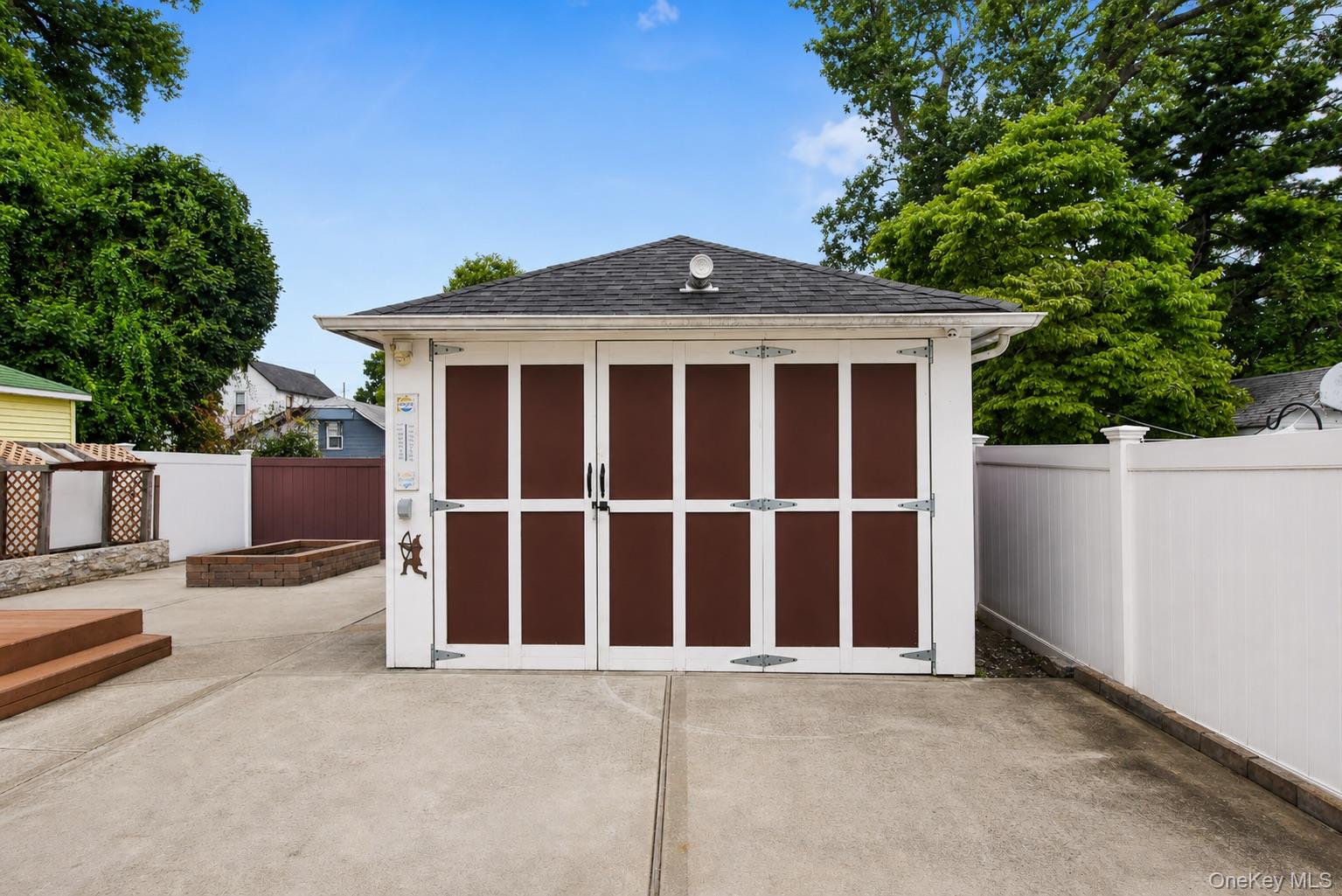 Detached garage with dark panel doors, a concrete driveway, and a white privacy fence