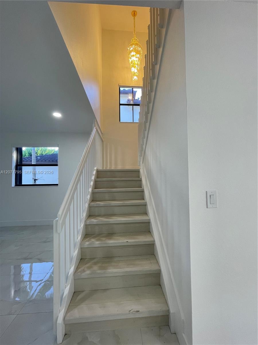 Staircase featuring white balusters and wood-finish treads, complemented by a multi-tiered crystal chandelier, recessed lighting, and large-format til