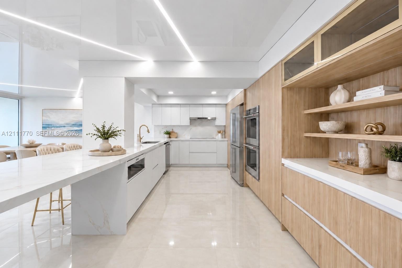 Contemporary kitchen featuring a sprawling waterfall-edge island, high-gloss flat-panel cabinetry, light-toned wood-finish cabinetry accents, integrat