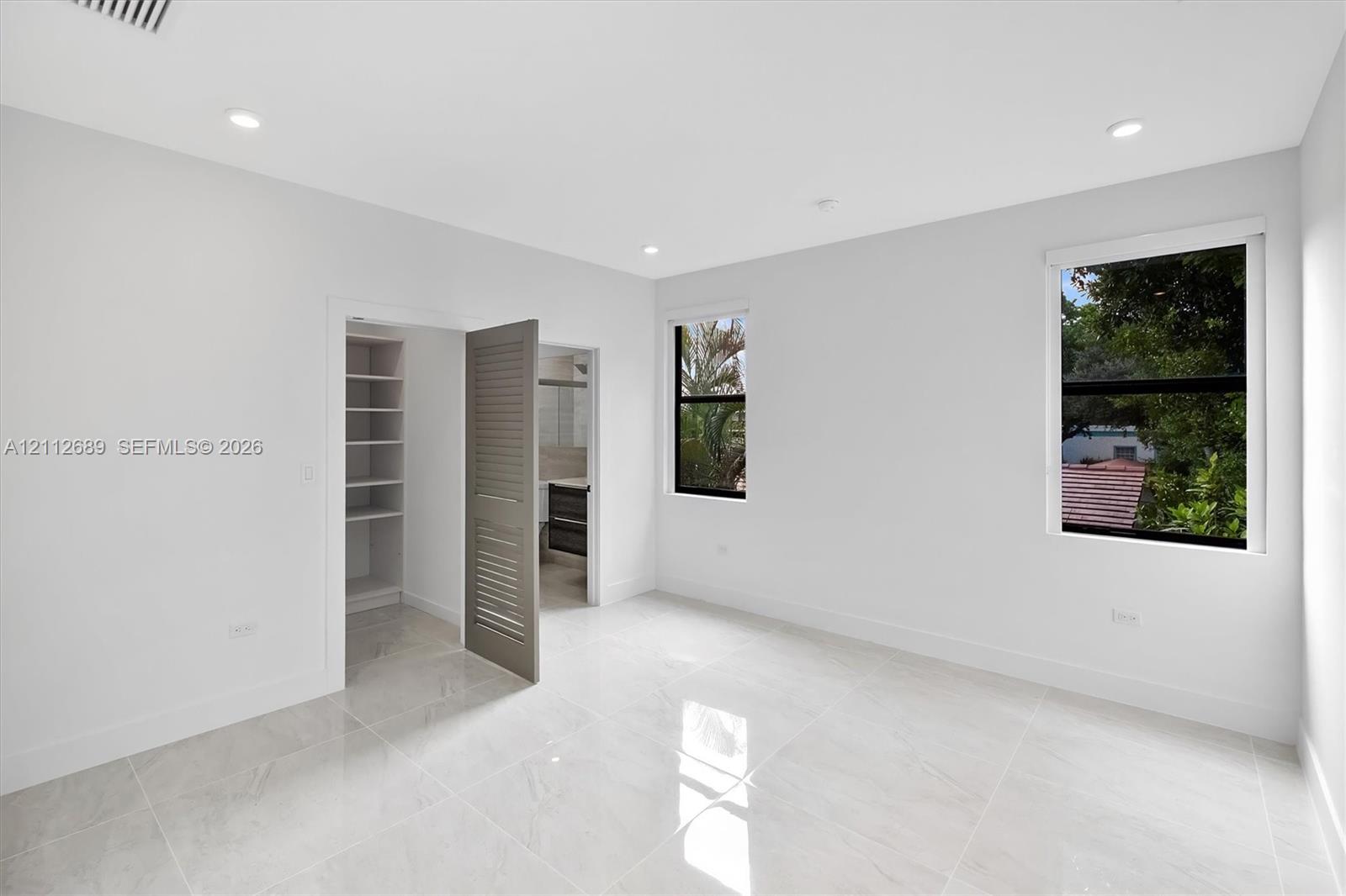 Interior space featuring polished porcelain tile flooring, recessed lighting, double-pane windows with black frames, and a walk-in closet with custom 