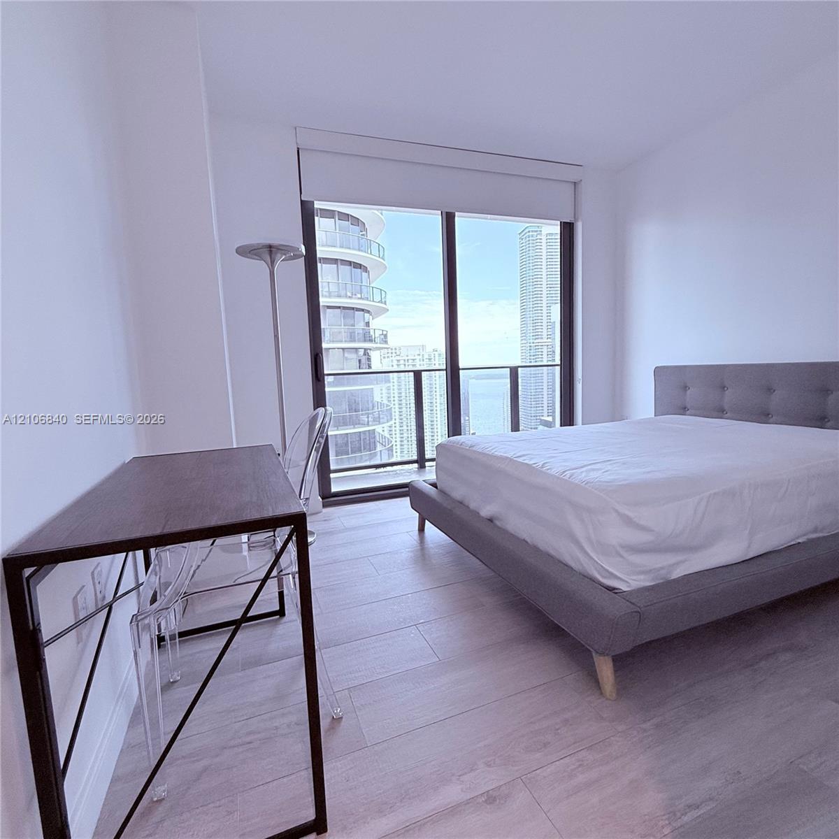 Floor-to-ceiling windows with roller shades, wood-finish flooring, and a private balcony featuring a glass-panel railing