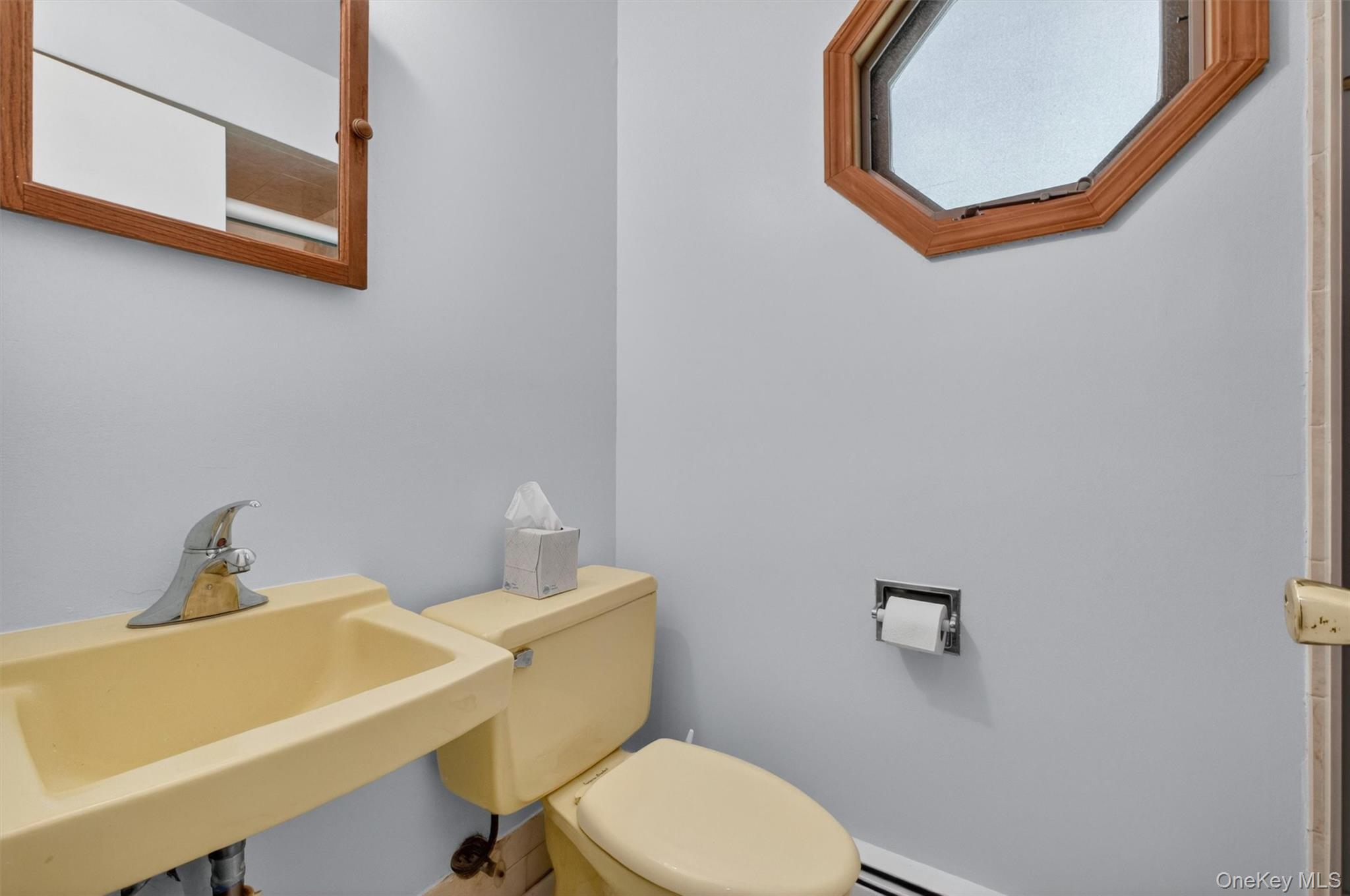 1st Fl. Full Bath featuring a wall-mounted sink, toilet, and an octagonal window with wood trim