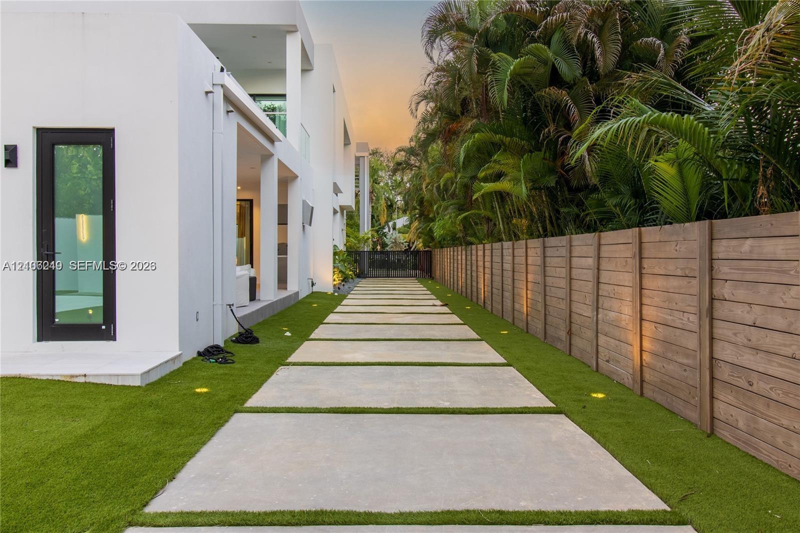 Modern exterior featuring smooth white stucco, a geometric concrete paver pathway, artificial turf landscaping, a horizontal wood-slat privacy fence, 