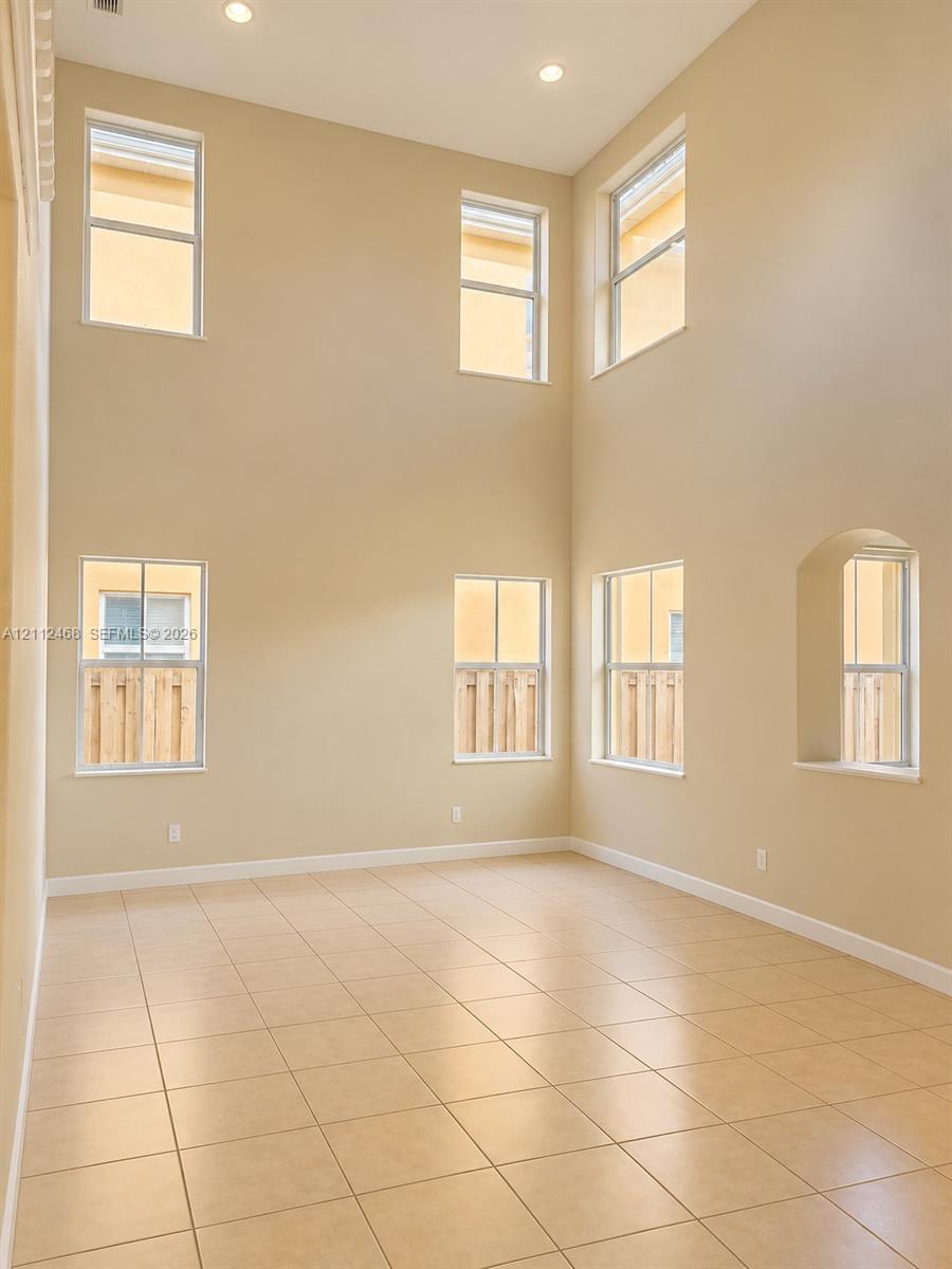 Double-height ceilings featuring recessed lighting, large-format tile flooring, and multiple window placements including a signature arched window