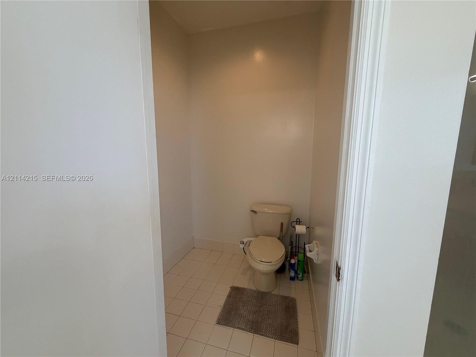 Enclosed water closet featuring light-toned tile flooring and neutral wall finishes