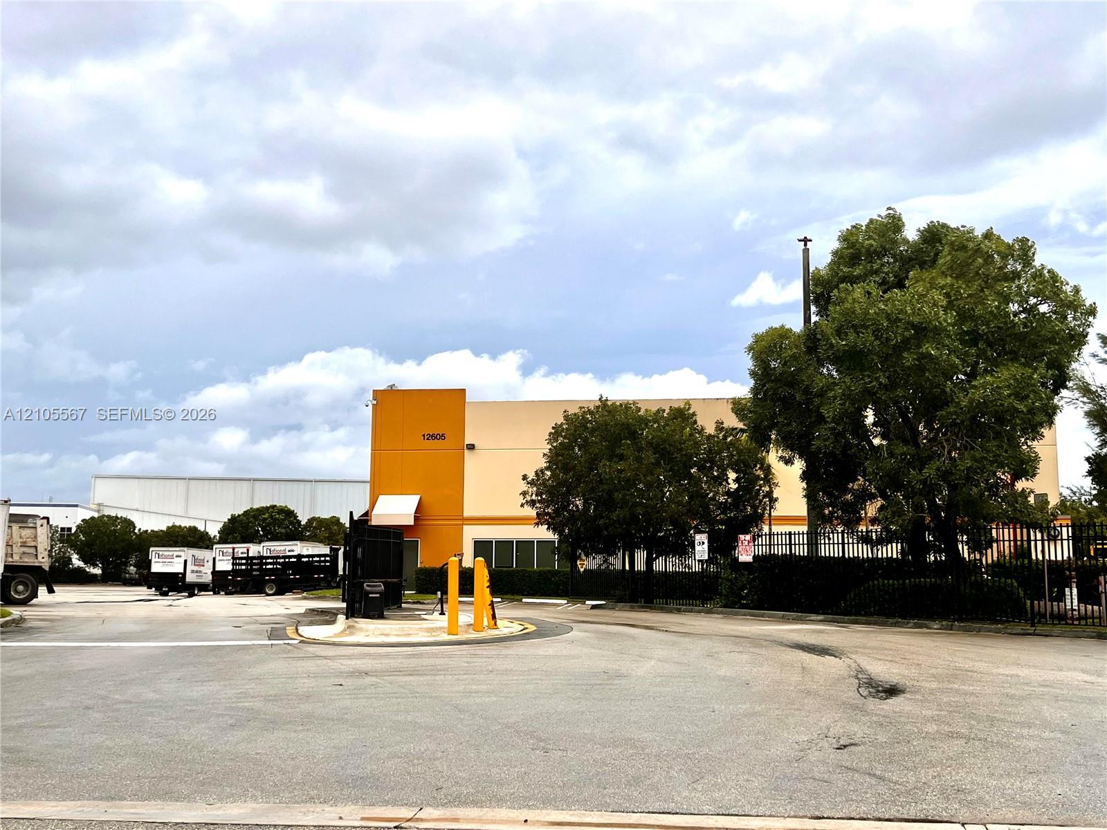 Industrial building with a tan and orange facade, featuring a prominent address number and a dark metal fence