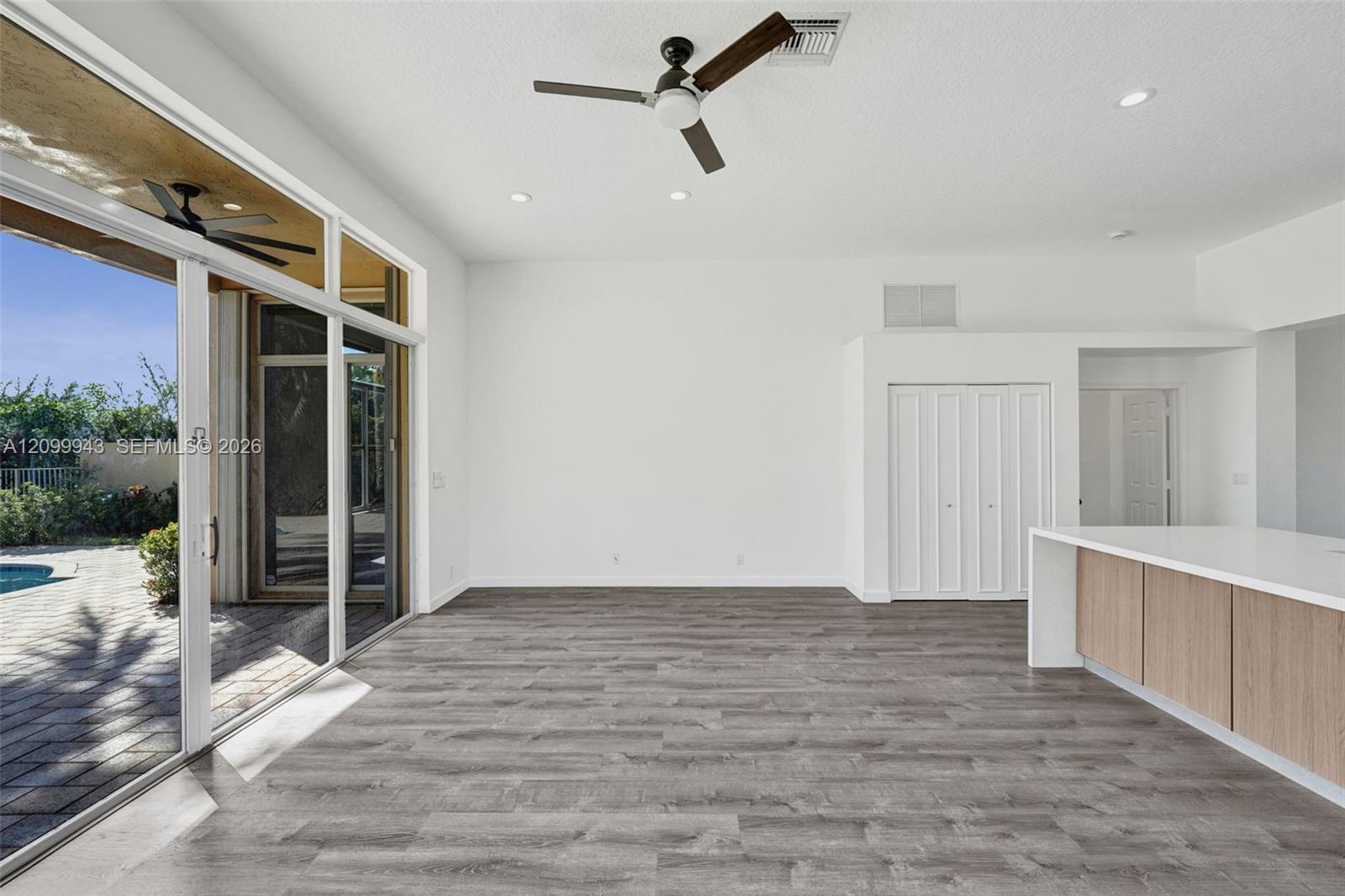 Open-concept space featuring wood-finish flooring, a kitchen island with stone-style countertop and light wood cabinetry, recessed lighting, and a mul