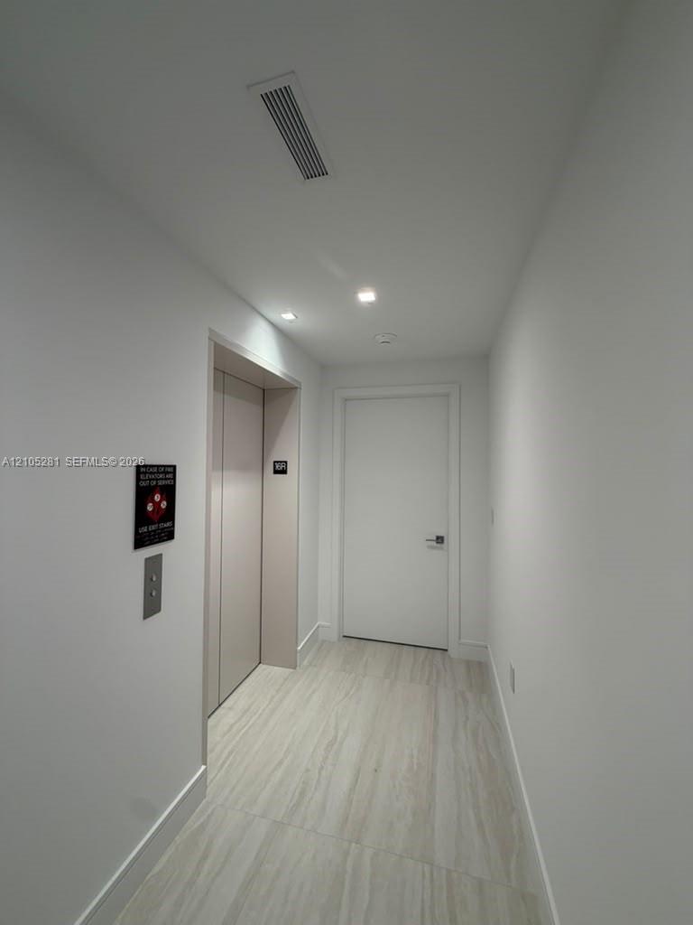 Neutral-toned hallway featuring wood-finish flooring, recessed ceiling lighting, and a private elevator entrance