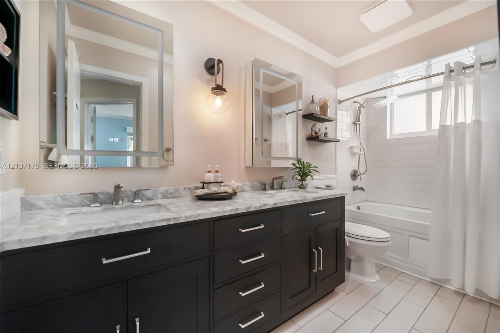 Hallway Bath. Double vanity featuring dark cabinetry, stone-finish countertops, lighted dual mirrored cabinets, wall-mounted lighting, and a bathtub-s