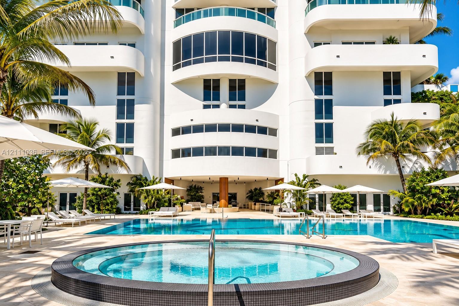 Multi-story exterior featuring curved balconies, floor-to-ceiling windows, a circular spa with tiled surround, a sprawling swimming pool, and stone pa