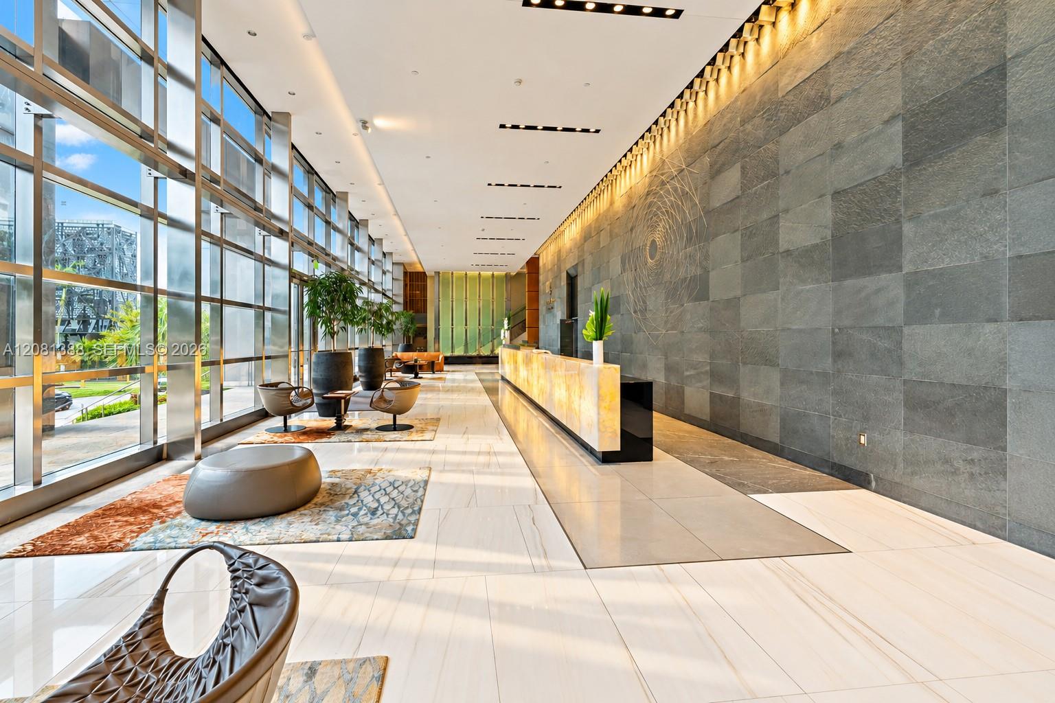 Grand lobby featuring floor-to-ceiling windows, large-format polished tile flooring, a prominent stone-tiled feature wall, recessed cove lighting, and