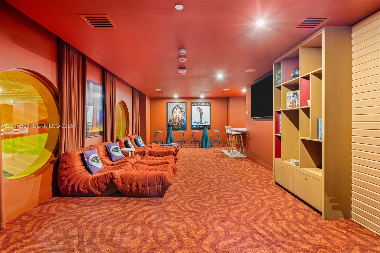Custom media room featuring circular wall accents, built-in floor-to-ceiling shelving with cabinetry, patterned wall-to-wall carpeting, and recessed c