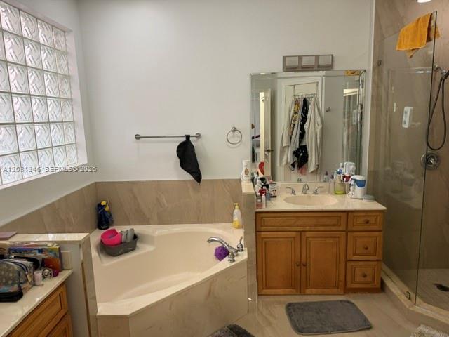 Built-in corner bathtub, glass block window, single vanity with wood cabinetry, large mirror, and glass-enclosed shower