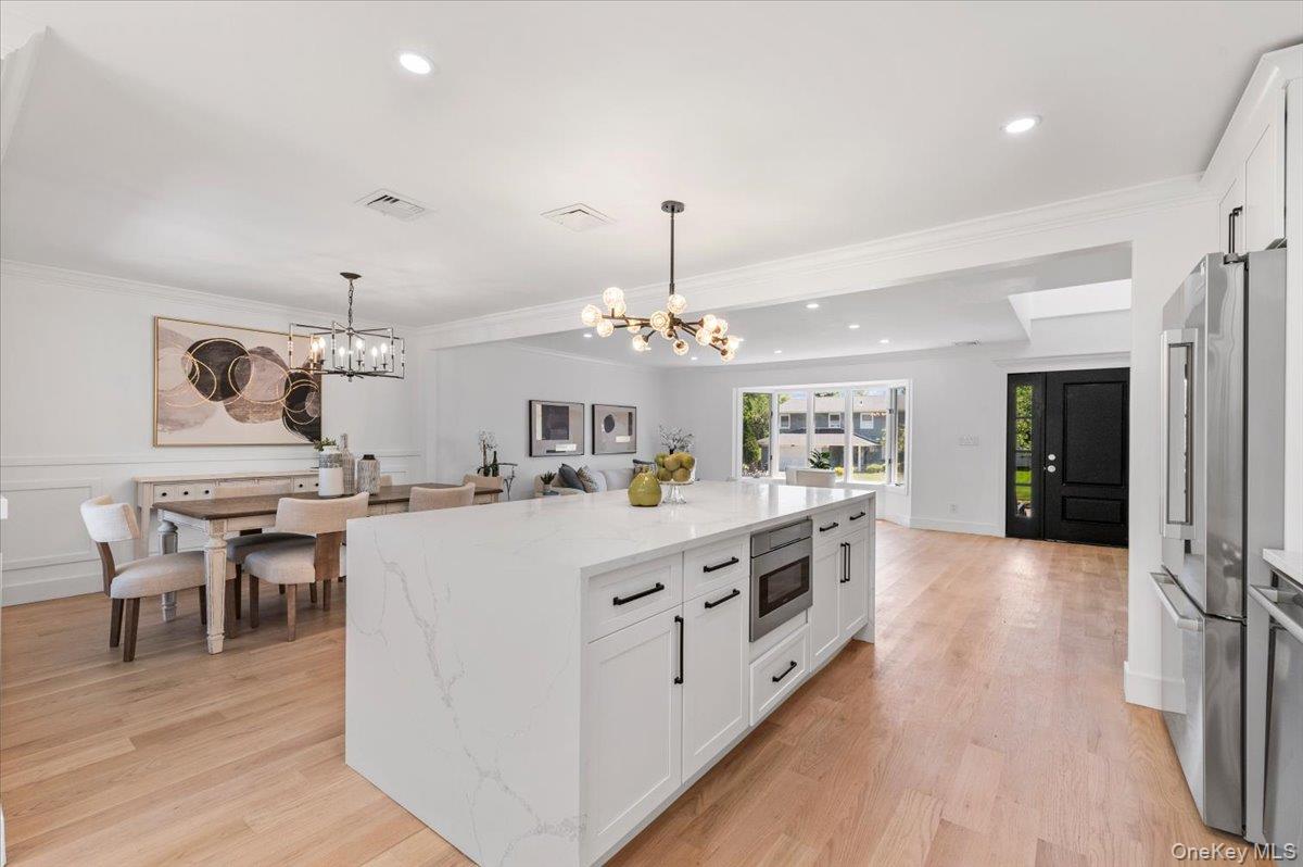 Kitchen featuring a chandelier, appliances with stainless steel finishes, white cabinetry, light stone countertops, and hanging light fixtures