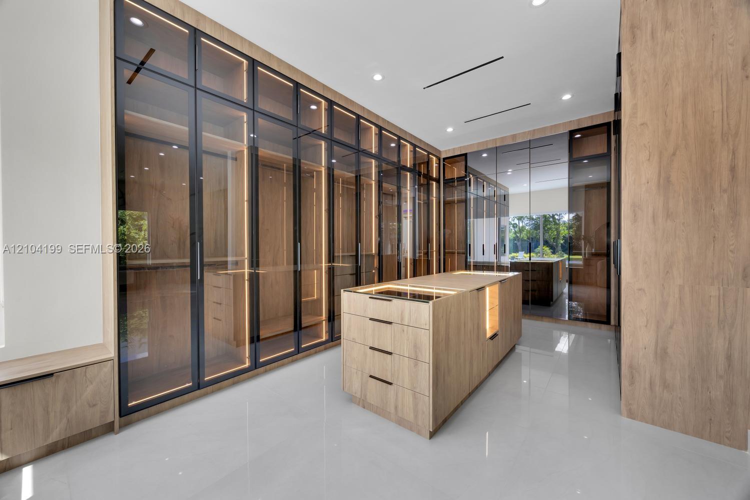 Custom storage system featuring floor-to-ceiling cabinetry with glass-panel doors, integrated LED lighting, central built-in island with storage drawe