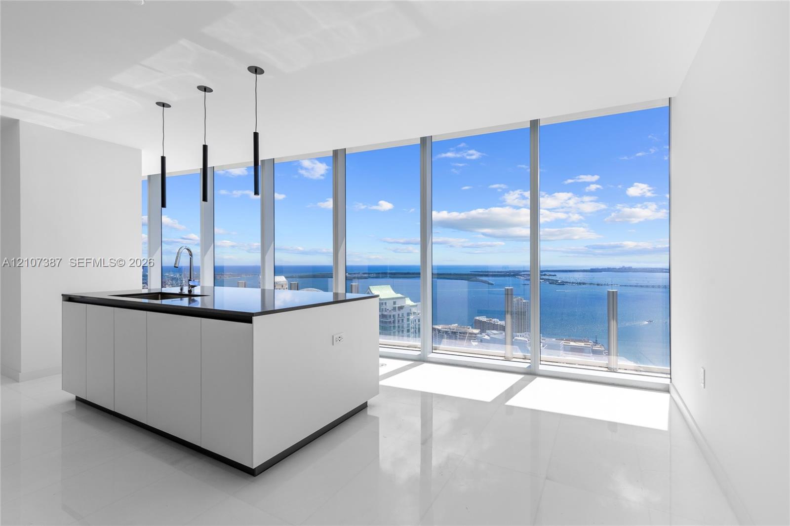 Kitchen island with a dark countertop and integrated sink, complemented by three modern pendant lights and floor-to-ceiling windows featuring coastal 