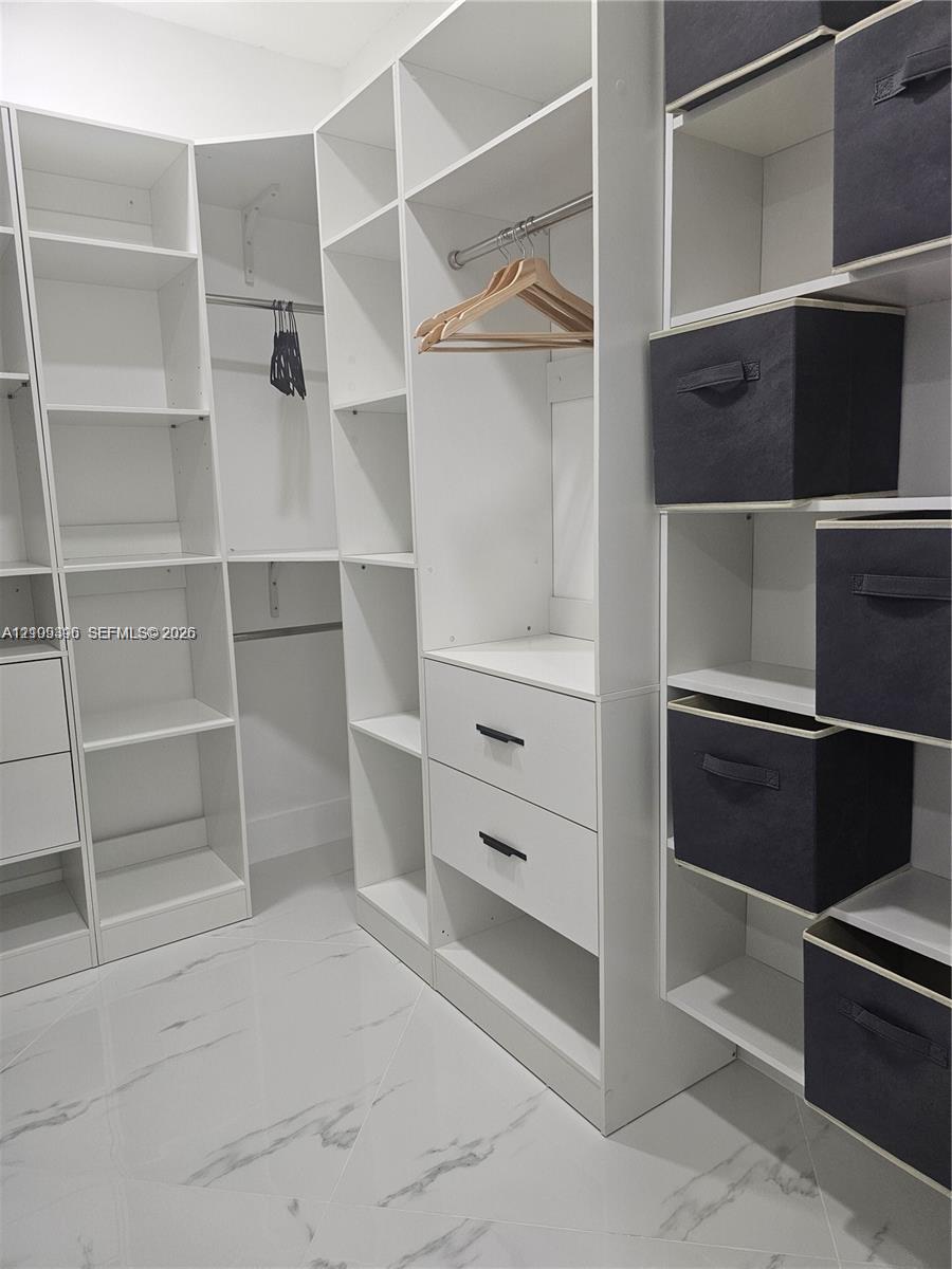 Custom reach-in closet featuring white floor-to-ceiling built-in shelving, integrated hanging rods, two soft-close drawers with matte black hardware, 