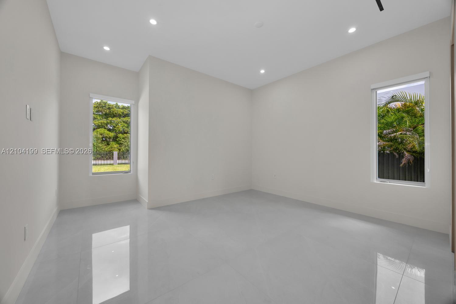 Neutral-toned interior room featuring large-format tile flooring, recessed ceiling lighting, and two windows providing natural illumination