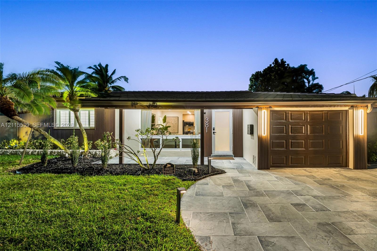 Single-story exterior featuring a natural stone-patterned paved driveway, integrated vertical exterior wall lighting, and landscaped front lawn with m