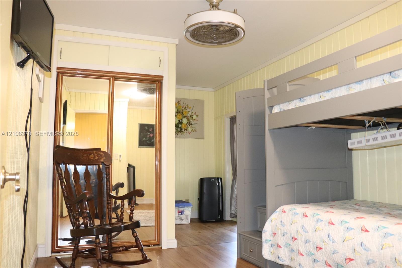 Wood-finish flooring, vertical panel wall detailing, mirrored sliding closet doors with built-in overhead storage, and a ceiling-mounted light fixture