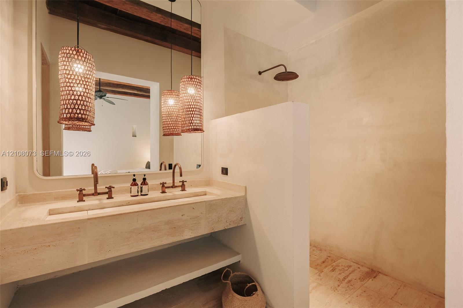 Stone-topped double vanity featuring an integrated trough sink, wall-mounted bronze-finish faucets, large rectangular mirror, and textured pendant lig