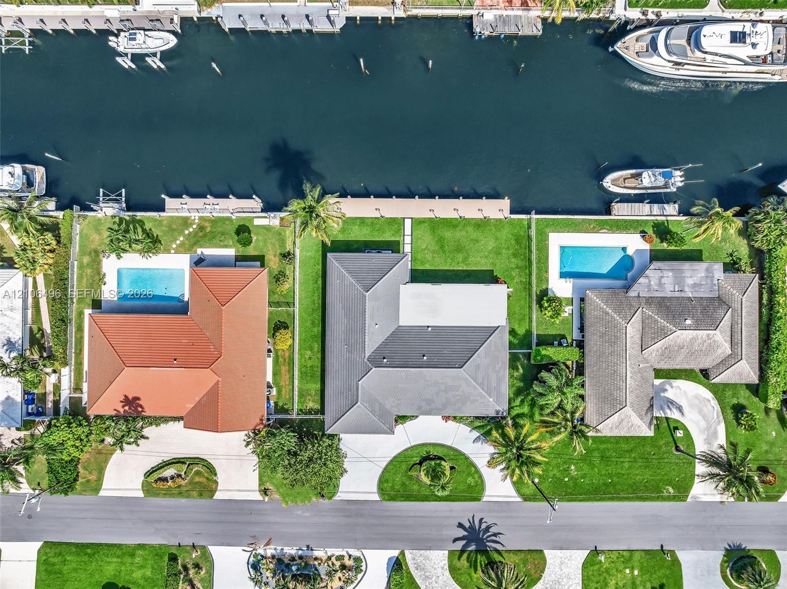 Waterfront property featuring a private boat dock, rectangular swimming pool, manicured lawn, and multi-faceted hipped roofline